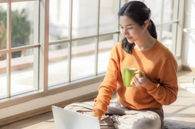Genç bir Asyalı iş kadını, Coronavirus salgınından sosyal uzaklık sırasında video konferans sistemi tarafından işletilen dizüstü bilgisayarını kullanarak evinde oturuyor..