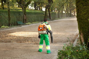 Bahçıvan şehir parkı içinde üfleyici sırt çantası ile üfleme yapraklar. Sonbahar konsepti