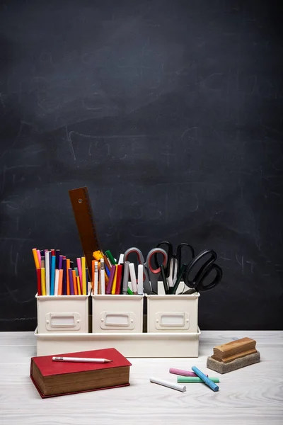 Torna a scuola sfondo con libro, matite, pastelli, gesso e altre forniture su lavagna nera — Foto Stock