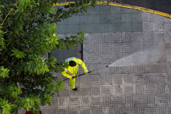 Worker cleaning the street sidewalk with high pressure water jet