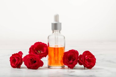 Cam şişedeki kokulu gül suyu ve yapraklı küçük kırmızı güller.