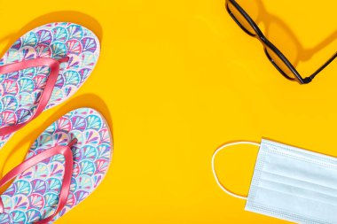 Düz kompozisyon, yaz tatili aksesuarları ve sarı arka planda yüz maskesi. Coronavirus covid-19 salgını sırasında yaz ya da tatil konsepti. Üst Manzara. Boşluğu kopyala