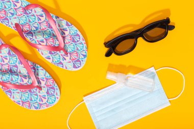 Düz kompozisyon, yaz tatili aksesuarları ve sarı arka planda yüz maskesi. Coronavirus covid-19 salgını sırasında yaz ya da tatil konsepti. Üst görünüm