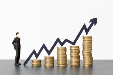 Artan madeni para yığınlarına bakan işadamı ve büyüyen grafik oku, iş büyümesi ve yatırım kavramına işaret ediyor