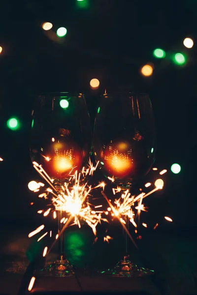 Pétillant Bengale pétillants bâtons en flammes sur un fond noir avec des lumières bokeh et verres à vin. Noël thème nouvel an fond. carte de vacances — Photo