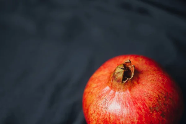 Reifer ganzer roter Granatapfel auf schwarzem Stoffhintergrund, Granatapfelkerne, Nahaufnahme, isoliertes Stillleben, orientalische Früchte — Stockfoto