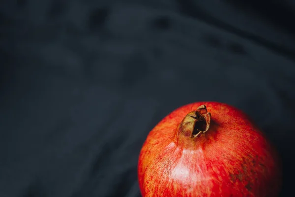 Reifer ganzer roter Granatapfel auf schwarzem Stoffhintergrund, Granatapfelkerne, Nahaufnahme, isoliertes Stillleben, orientalische Früchte — Stockfoto