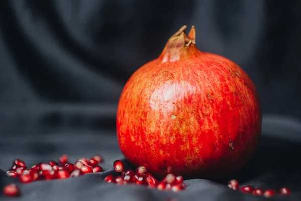 Reifer ganzer roter Granatapfel auf schwarzem Stoffhintergrund, Granatapfelkerne, Nahaufnahme, isoliertes Stillleben, orientalische Früchte — Stockfoto