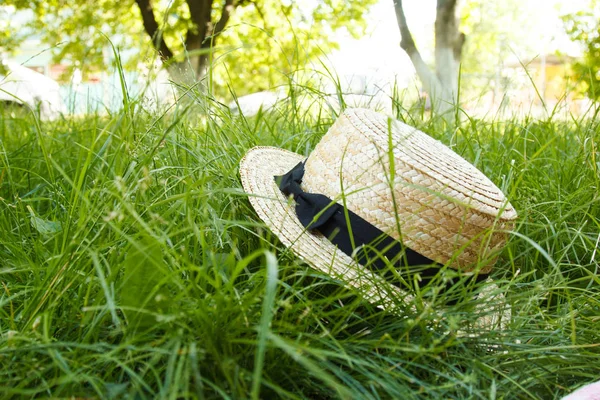 En stråhatt liggande på gräset utomhus med en gul citrus frukt och en flaska saft. Picknick på naturen i parken på en bakgrund av träd med strålande solsken — Stockfoto