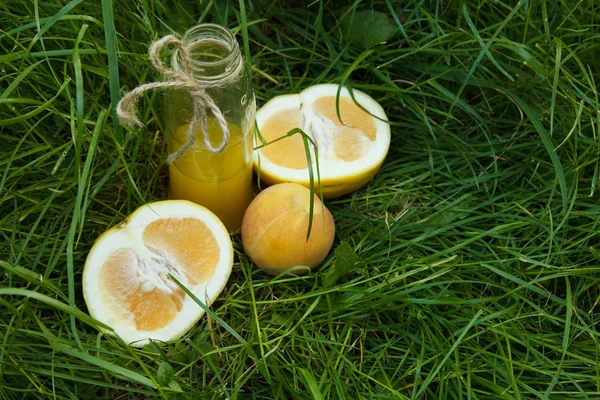 Бутылка домашнего лимонадного сока лежит на траве на открытом воздухе. Пикник на природе в парке на фоне деревьев с ярким солнцем. здоровое питание, питание — стоковое фото