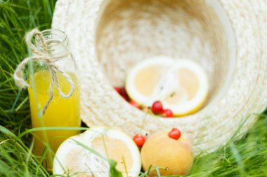 ev yapımı limonata suyu kiraz ve narenciye meyve ile açık havada çim üzerinde yalan hasır şapka ile bir şişe şişe. Doğa Park piknik sağlıklı gıda, beslenme, kişisel bakım kadar kapatın. güneşli gün.