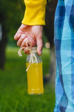 adam onun el şişe ağaçlar park ve yeşil çim zemin üzerine ev yapımı limonata tutar. güneşli bir gün, yaz. portre. Piknik sağlıklı gıda taze. kırpılmış görüntü