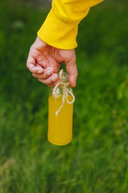 adam onun el şişe ağaçlar park ve yeşil çim zemin üzerine ev yapımı limonata tutar. güneşli bir gün, yaz. portre. Piknik sağlıklı gıda taze. kırpılmış görüntü