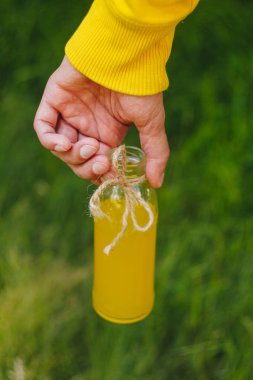 adam onun el şişe ağaçlar park ve yeşil çim zemin üzerine ev yapımı limonata tutar. güneşli bir gün, yaz. portre. Piknik sağlıklı gıda taze. kırpılmış görüntü