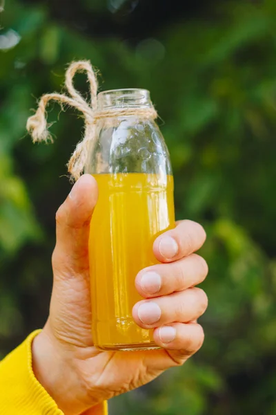 Man holds in his hand bottle of homemade lemonade on the background of trees in the park and green grass. sunny day, summer. closeup. picnic healthy food fresh. cropped image — Stock Photo, Image
