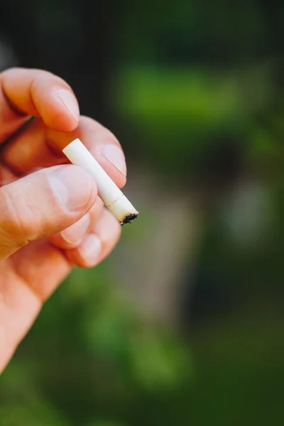 Cigareta nezanikne v ruce muže s vousy na přírodu na pozadí zelených stromů. Nikotin filtr. Nezdravý životní styl. Detail. nedopalek. Macrophoto — Stock fotografie