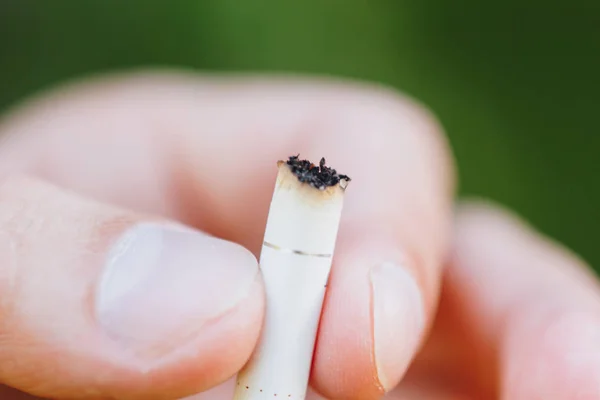 Cigarrillo extinguido en su mano un hombre con una barba en la naturaleza sobre el fondo de árboles verdes. Filtro de nicotina. Estilo de vida insalubre. Primer plano. colilla de cigarrillos. Macrofoto — Foto de Stock