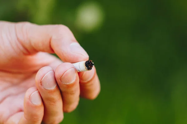 香烟熄灭在他的手上一个人与自然在绿色树木的背景下的胡子。尼古丁过滤器不健康的生活方式。特写。烟头。宏照片 — 图库照片