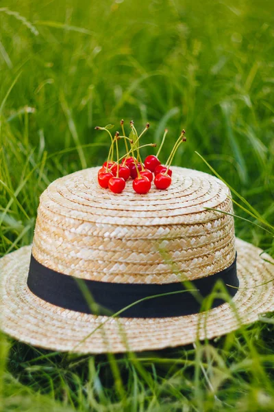 Несколько спелых фруктов сладкой вишни с веткой на соломенной шляпе, лежащей на траве на открытом воздухе. Пикник на природе в парке закрывает здоровую пищу, диету, уход за собой. солнечный день . — стоковое фото