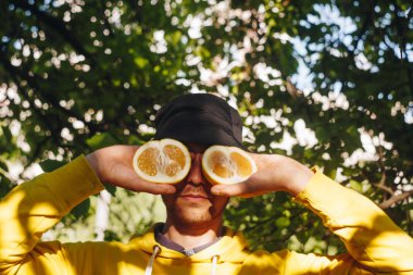 sarı hoodie ve mavi Panama bir adam gözleri önce yarım sarı bir narenciye kesilmiş iki yarısı tutuyor. sağlıklı yeme, uygun beslenme, organik gıda, yakın çekim