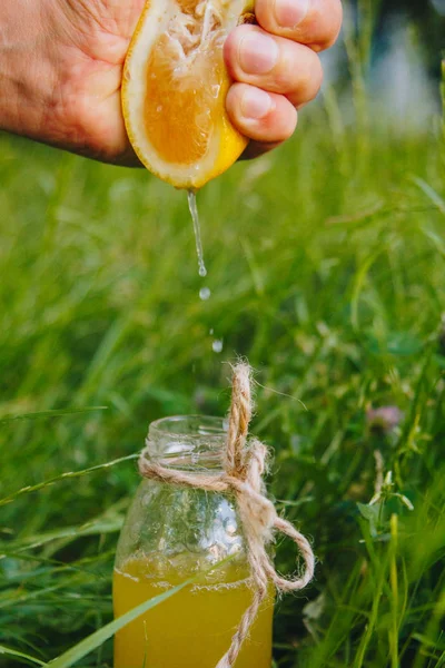male hand squeezes citrus fruit juice into a bottle of homemade lemonade on the grass on the nature outdoors. close-up, healthy food, diet, proper nutrition, picnic.