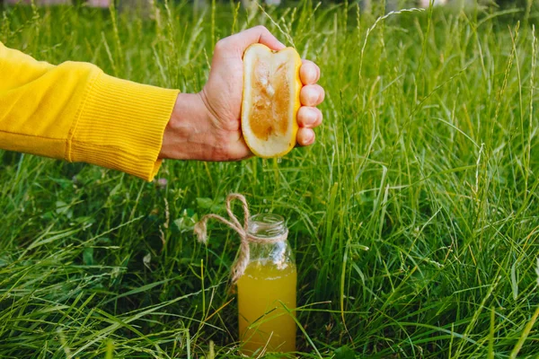 Мужская рука сжимает цитрусовый сок в бутылку домашнего лимонада на траве на природе. крупный план, здоровое питание, диета, правильное питание, пикник . — стоковое фото