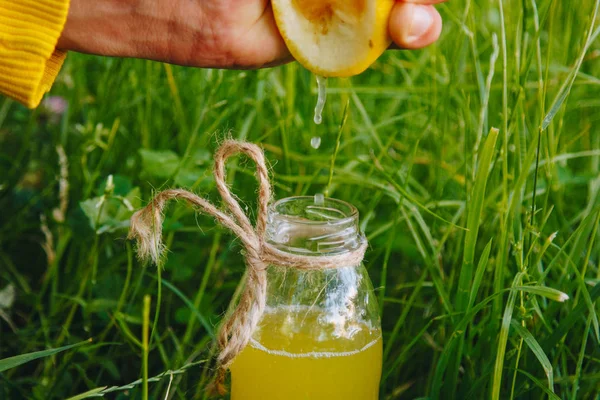 Male hand squeezes citrus fruit juice into a bottle of homemade lemonade on the grass on the nature outdoors. close-up, healthy food, diet, proper nutrition, picnic. — Stock Photo, Image