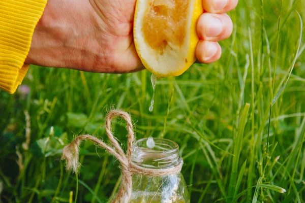 Male hand squeezes citrus fruit juice into a bottle of homemade lemonade on the grass on the nature outdoors. close-up, healthy food, diet, proper nutrition, picnic. — Stock Photo, Image