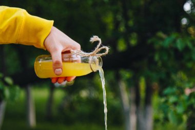 Erkek el doğal açık havada ağaçların bir arka planda bir şişe ev yapımı limonata dökülen. yakın çekim, sağlıklı gıda, diyet, uygun beslenme, piknik. Yaz.