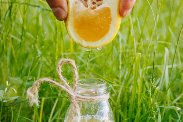 male hand squeezes citrus fruit juice into a bottle of homemade lemonade on the grass on the nature outdoors. close-up, healthy food, diet, proper nutrition, picnic.