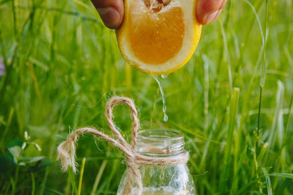 male hand squeezes citrus fruit juice into a bottle of homemade lemonade on the grass on the nature outdoors. close-up, healthy food, diet, proper nutrition, picnic.