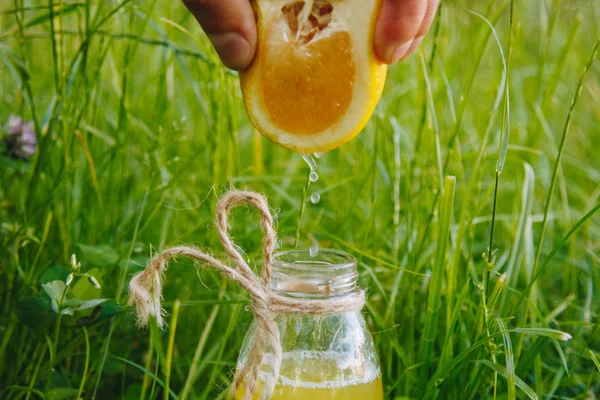 male hand squeezes citrus fruit juice into a bottle of homemade lemonade on the grass on the nature outdoors. close-up, healthy food, diet, proper nutrition, picnic.