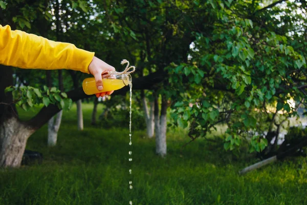 Male hand giet zelfgemaakte limonade uit een fles op een achtergrond van bomen op de natuur buitenshuis. Close-up, gezonde voeding, dieet, goede voeding, picknick. Zomer. — Stockfoto