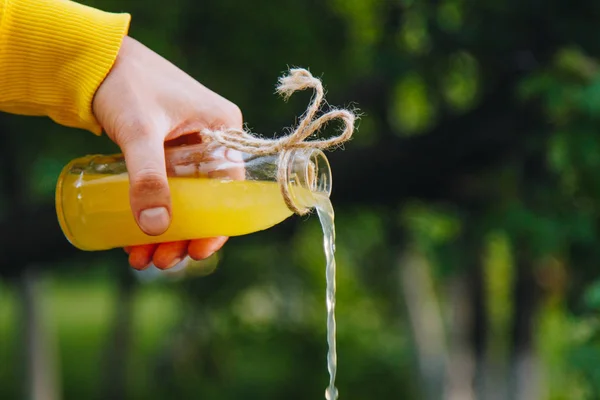 Male hand pours homemade lemonade from a bottle on a background of trees on the nature outdoors. close-up, healthy food, diet, proper nutrition, picnic. Summer. — Stock Photo, Image