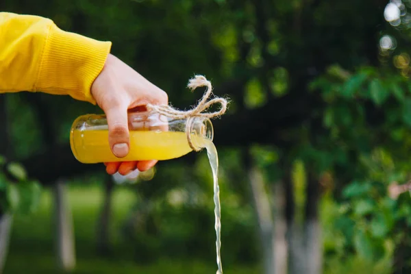 Male hand pours homemade lemonade from a bottle on a background of trees on the nature outdoors. close-up, healthy food, diet, proper nutrition, picnic. Summer. — Stock Photo, Image
