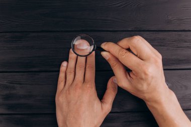 bir büyüteç tutan rustik bir siyah masa üzerinde erkek elleri. parmak izi muayenesi. palmiye çekim.