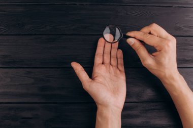 bir büyüteç tutan rustik bir siyah masa üzerinde erkek elleri. parmak izi muayenesi. palmiye çekim.