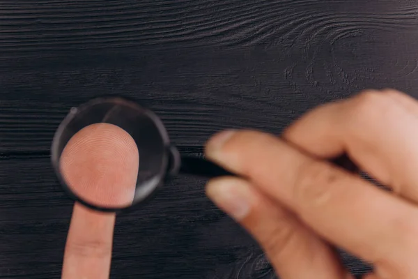Ανδρικά χέρια σε ένα ρουστίκ μαύρο γραφείο που κρατά ένα μεγεθυντικό φακό. εξέταση δακτυλικών αποτυπωμάτων. κοντινό πλάνο. — Φωτογραφία Αρχείου