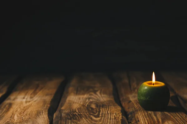 Lonely green ball-shaped candle burns on a rustic wooden table close-up — Stock Photo, Image