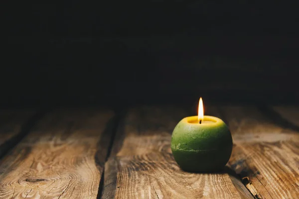 Lonely green ball-shaped candle burns on a rustic wooden table close-up — Stock Photo, Image