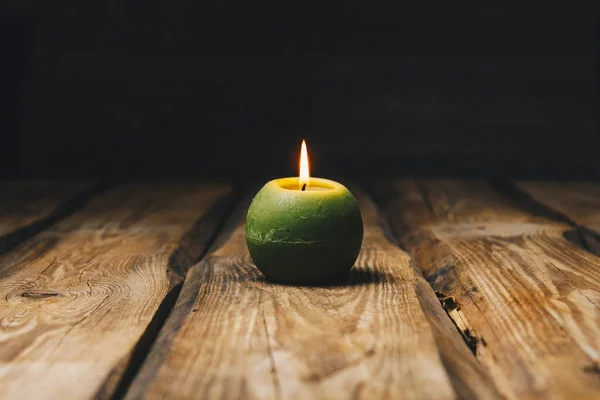 Lonely green ball-shaped candle burns on a rustic wooden table close-up — Stock Photo, Image