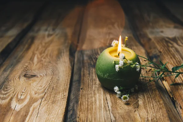 Одна зеленая свеча в форме шара с сухим цветком, горящим на деревенском деревянном столе крупным планом — стоковое фото