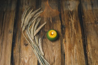 A single green ball-shaped candle with a spikelet of wheat is burning on a rustic wooden table close-up. top view clipart