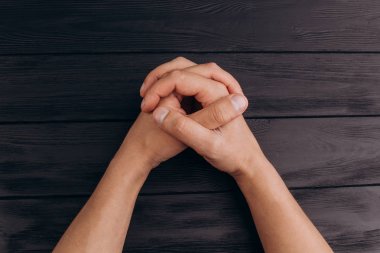 kilitli parmaklar, beyaz erkek elleri siyah rustik ahşap masa yakın kilitli. üst görünüm. Bir adam müzakereleri bekliyor