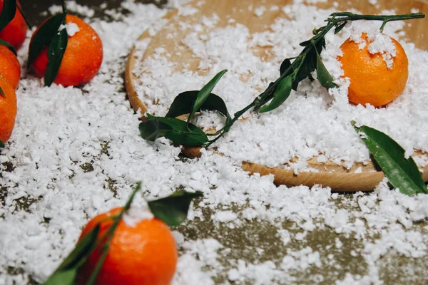 Bulanık bir arka plan üzerinde ahşap bir mutfak masasında yaprakları ile Mandalina narenciye. sağlıklı gıda. çiğ gıda Yapay beyaz kar. Yeni yıl. Noel