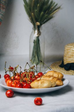 healthy light breakfast. sweet cherry with croissants on a plate. bouquet in a vase with spikelets of wheat. Straw hat. proper nutrition for a slim figure. raw foods vegetarianism. diet
