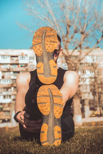 Piernas de atleta en leggings y zapatillas de deporte, acostado en el suelo en el césped de cerca. piernas cruzadas. entrenamiento al aire libre. calentamiento, estiramiento —  Fotos de Stock