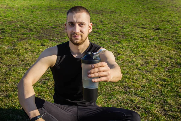 muscular slender man in training at the stadium drinks water from a sports shaker. recreation sports. athletic exercising