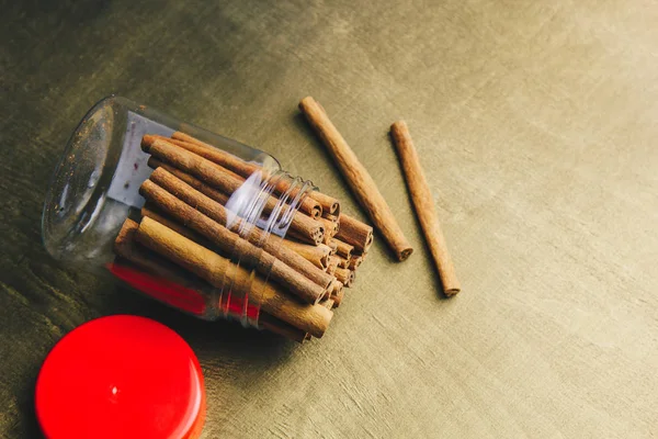 Whole sticks of fragrant cinnamon are tightly packed in a transparent jar with a red lid on a wooden rural table. copyspace. composition of seasoning and flavoring aromatic spice — Stock Photo, Image