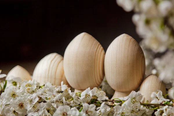Ostereier aus Holz zwischen blühenden Kirschzweigen auf einem rustikalen Tisch. symbolische Zusammensetzung der Frühlingsfeiertage für eine Geschenkkarte. Kopierraum. Nahaufnahme. Blütenblätter weißer Blüten. die Wiedergeburt der Natur — Stockfoto